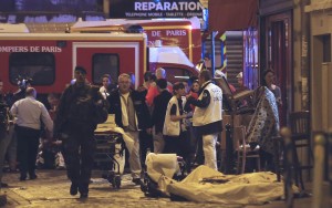 Policiais e bombeiros trabalham ao lado de corpos de vítimas de tiroteio que foram cobertos na calçada em frente a um restaurante de Paris, na França (Foto: Jacques Brinon/AP)