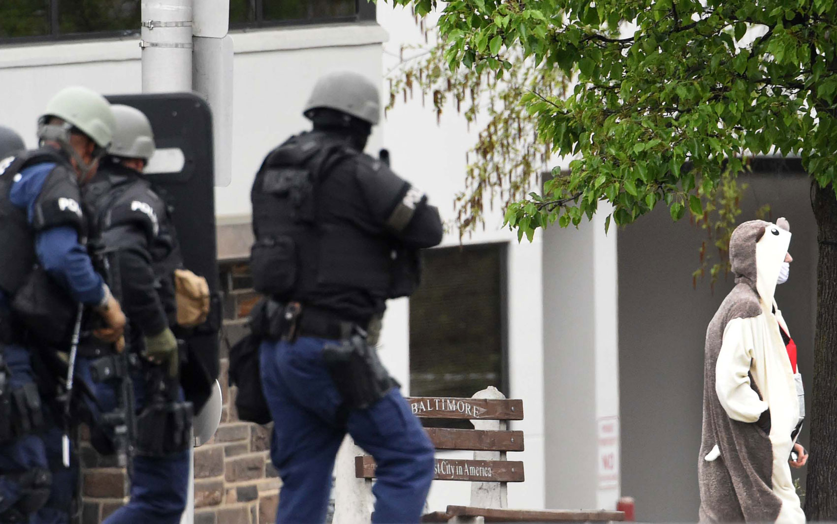 Homem com fantasia de animal e máscara cirúrgica que ameaçou detonar uma bomba é escoltado pela polícia para fora da sede de uma emissora de TV em Baltimore, na quinta (28) (Foto: Kenneth K. Lam/The Baltimore Sun via AP)