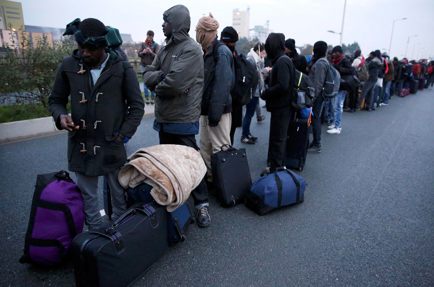 Migrantes fazem fila nesta segunda-feira (24) para aguardar a transferência do acampamento de Calais, no norte da França, para centros de acolhida espalhados pelo país (Foto: Neil Hall/ Reuters)